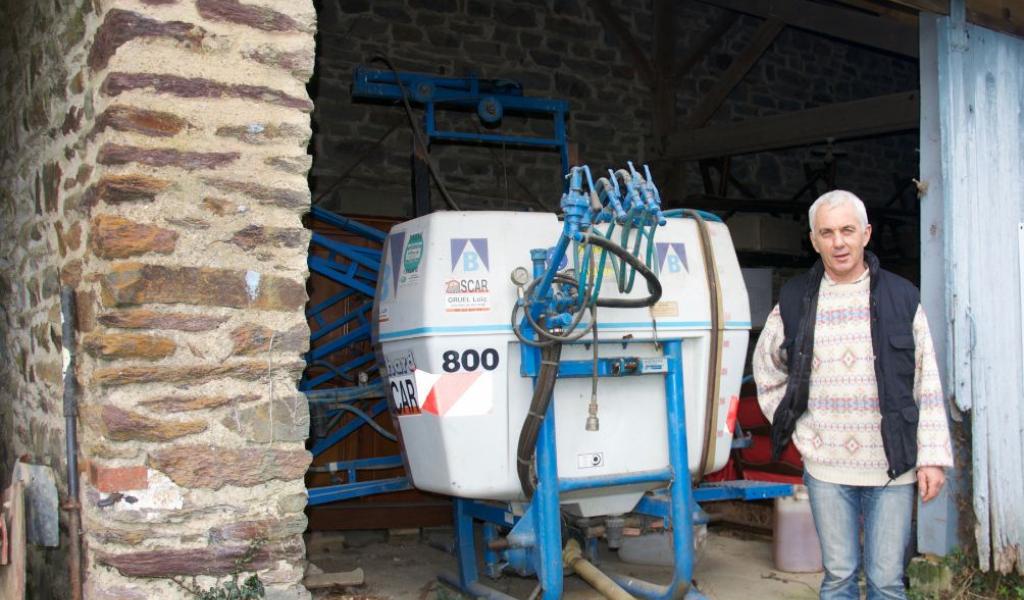 Armel Richomme à côté de son ancien pulvérisateur. Il ne se protégeait pas toujours quand il traitait, comme avec ce colorant nitré, l’Herbogil : « Sans les gants, on avait les mains toutes jaunes et elles restaient comme ça plusieurs jours. On avait beau savonner et frotter, c’était un produit tenace. » - Crédit : E.Veyssié